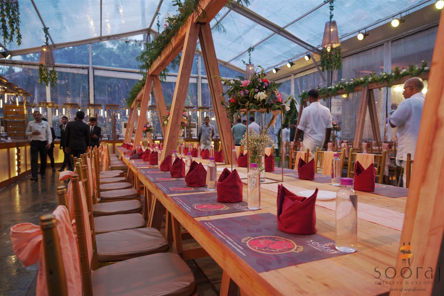 A banquet table under a glass canopy, set with wine-red napkins